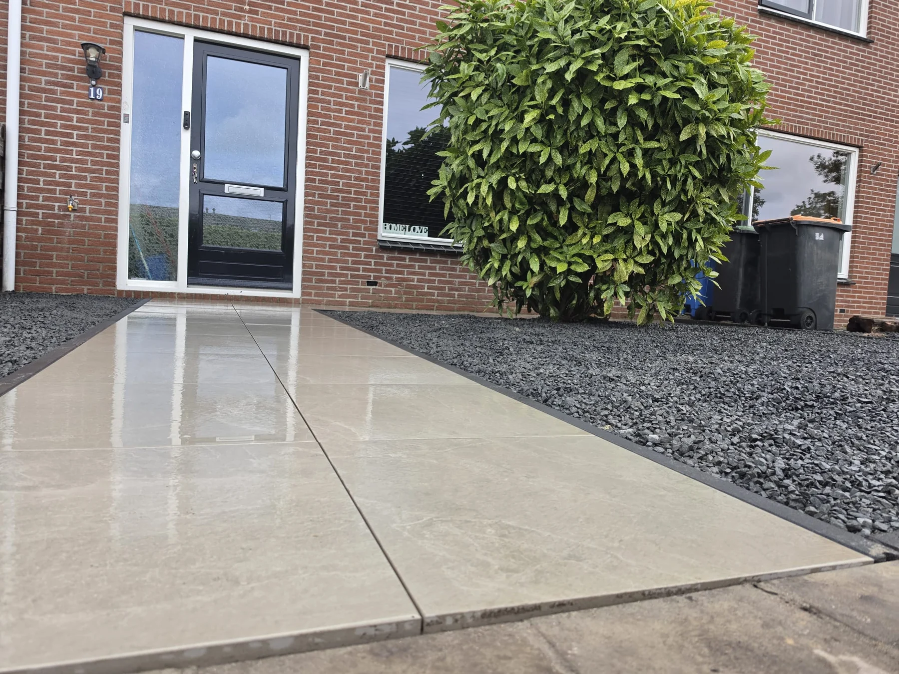 Grootformaat tegelpad met donkere siergrindvakken bij een voortuin