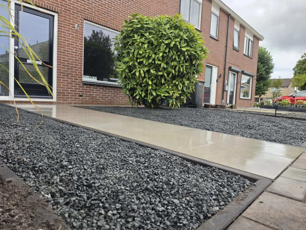 Laag zijaanzicht van een lang tegelpad met donkere siergrindvakken langs de woning
